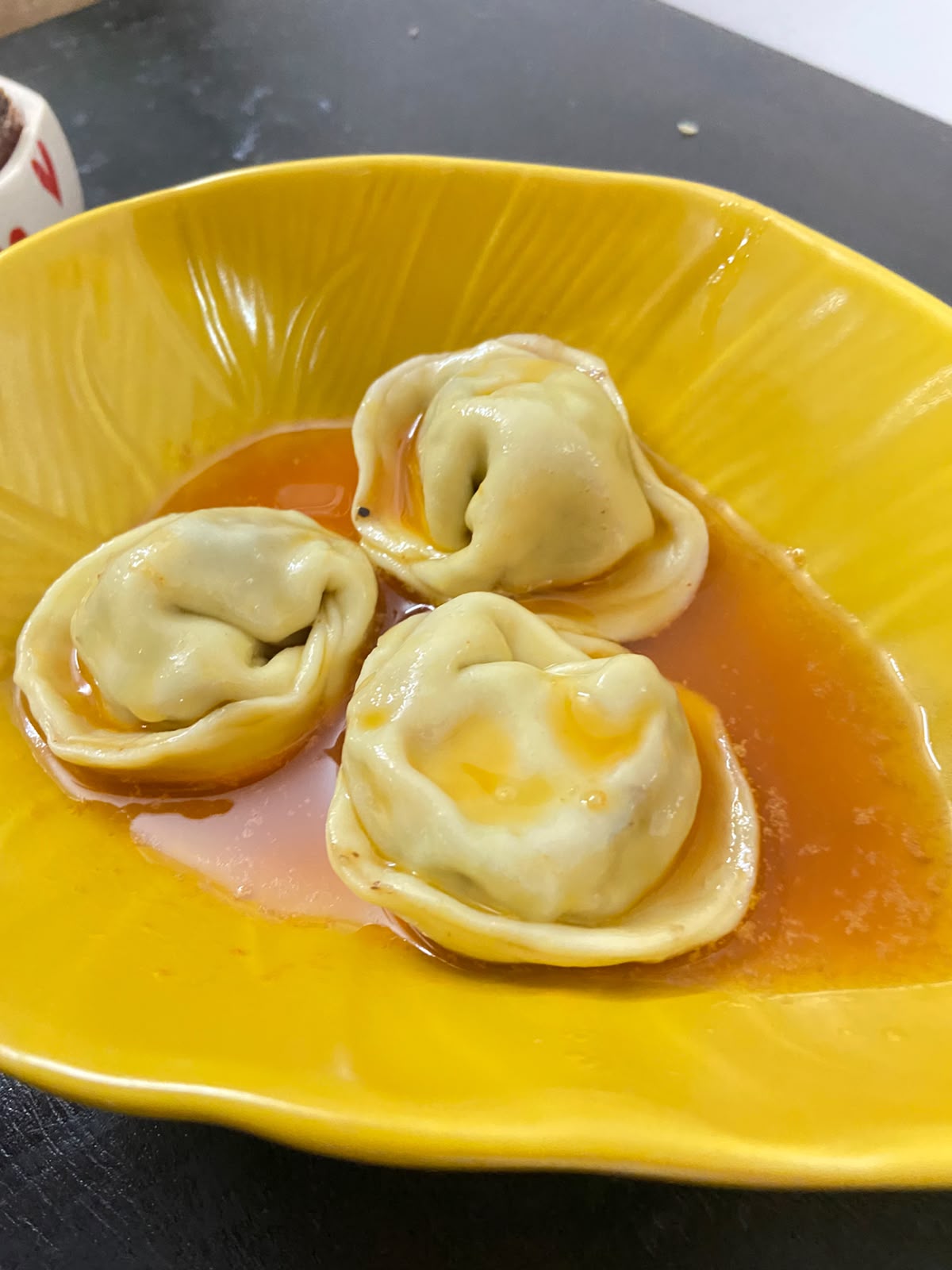Three prawn and taro tortellini sitting in chilli oil in a yellow bowl