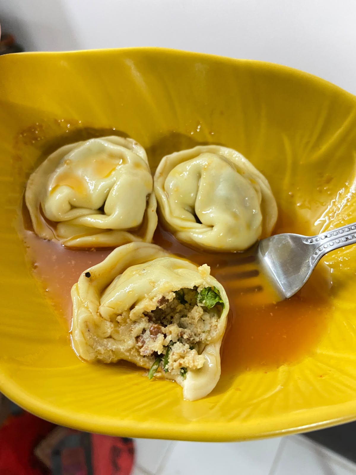 A tortellini bitten open, showing the prawn and taro filling with herbs